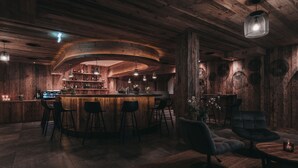 A rustic bar area with wooden walls, a curved bar counter, and several stools. - VAYA Galtür Paznaun (Galtur)