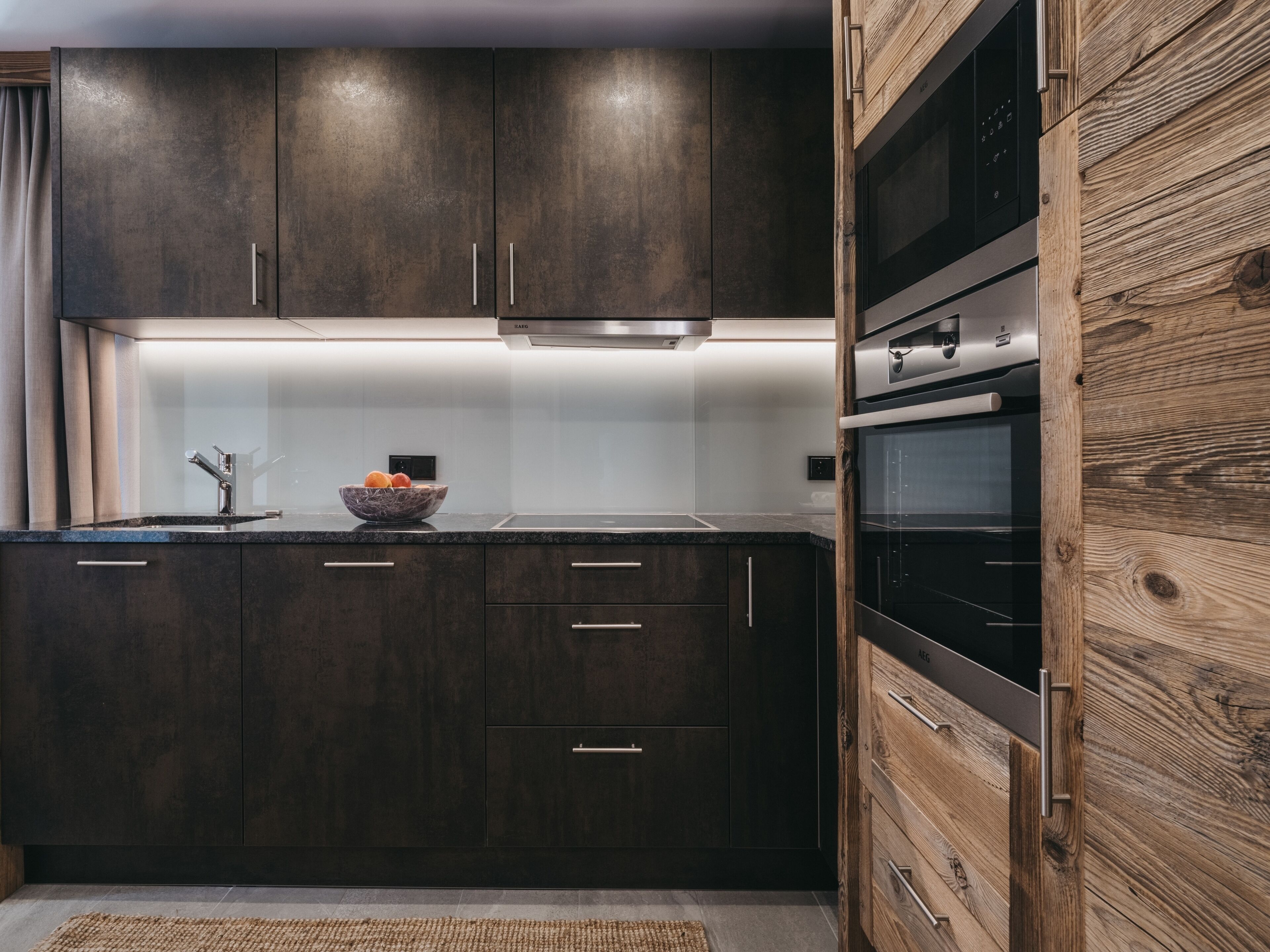 Una cucina moderna con mobili in legno scuro, lavello in acciaio inossidabile e forno integrato.