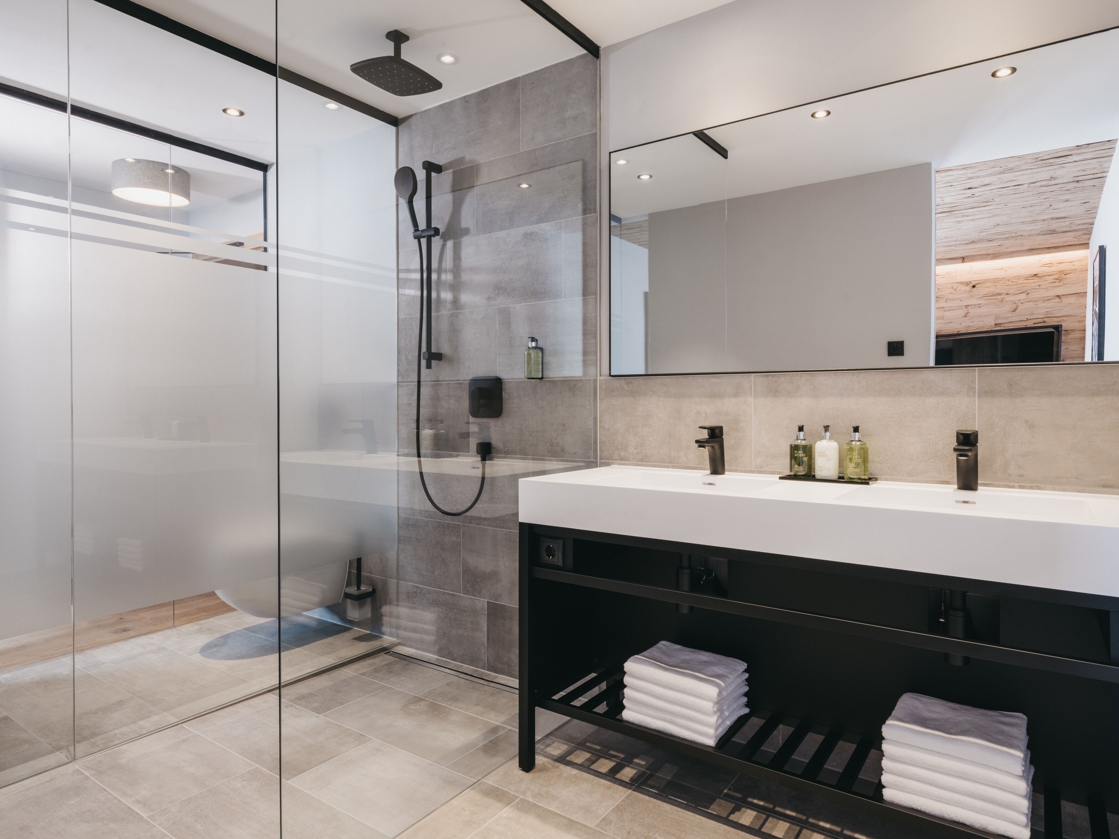 A modern bathroom with a glass shower enclosure, a large mirror, and a vanity with a sink and towel rack.
