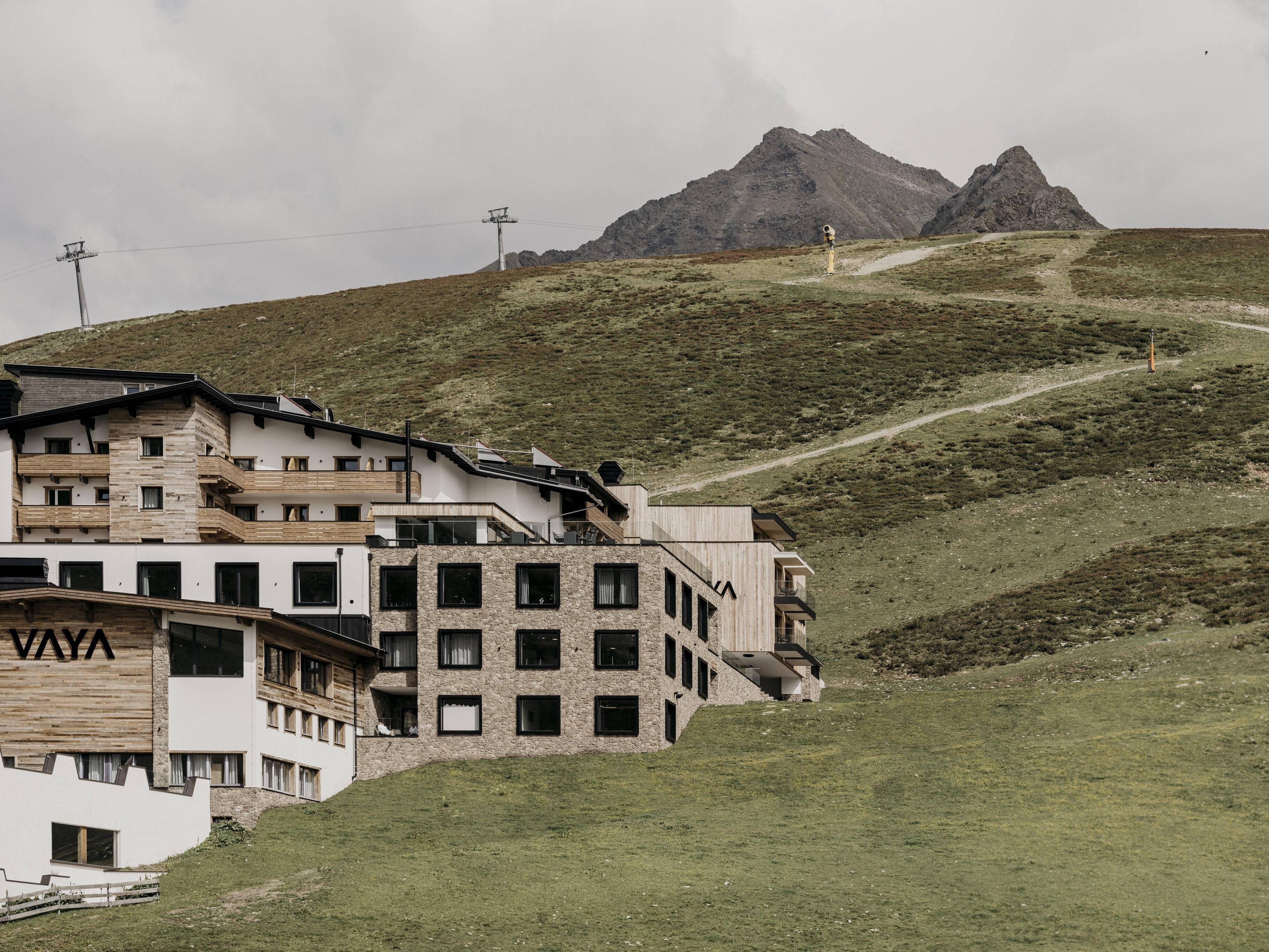 Un hôtel moderne à plusieurs étages, doté d’une façade en pierre et offrant une vue sur une chaîne de montagnes.