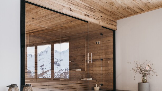 A modern interior with wooden panel walls, a glass door leading to a mountain view, and a minimalist decor including a potted plant and two candle holders. - VAYA Kühtai (Silz)
