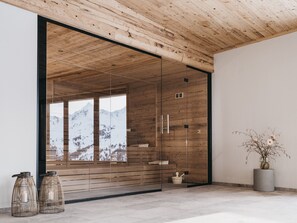 Un interior moderno con paneles de madera, una puerta de cristal que da a vistas de la montaña y una decoración minimalista que incluye una planta en maceta y dos candelabros.