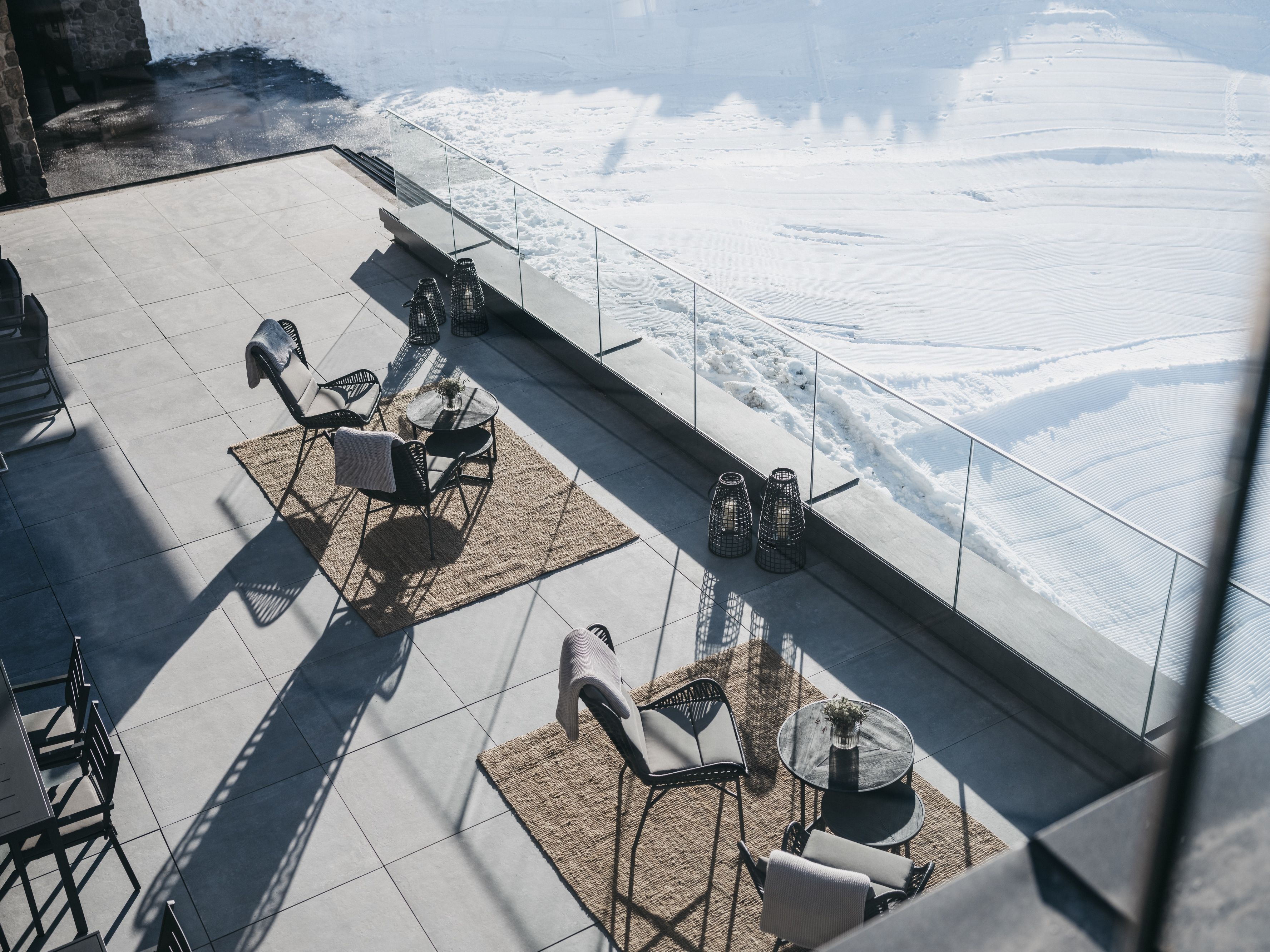 A rooftop terrace with outdoor seating, a glass railing, and a view of a snowy landscape.