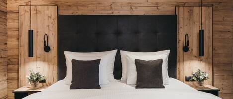 A bedroom with a wooden ceiling, a tufted headboard, two bedside tables with lamps, and a bed with white and dark pillows.