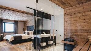 A modern bedroom with a large bed, a glass partition, a wooden bench, and a sauna area. - VAYA Kühtai (Silz)
