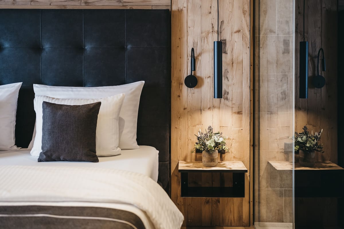 A modern bedroom with a dark headboard, white bedding, and a wooden nightstand with a vase of flowers.
