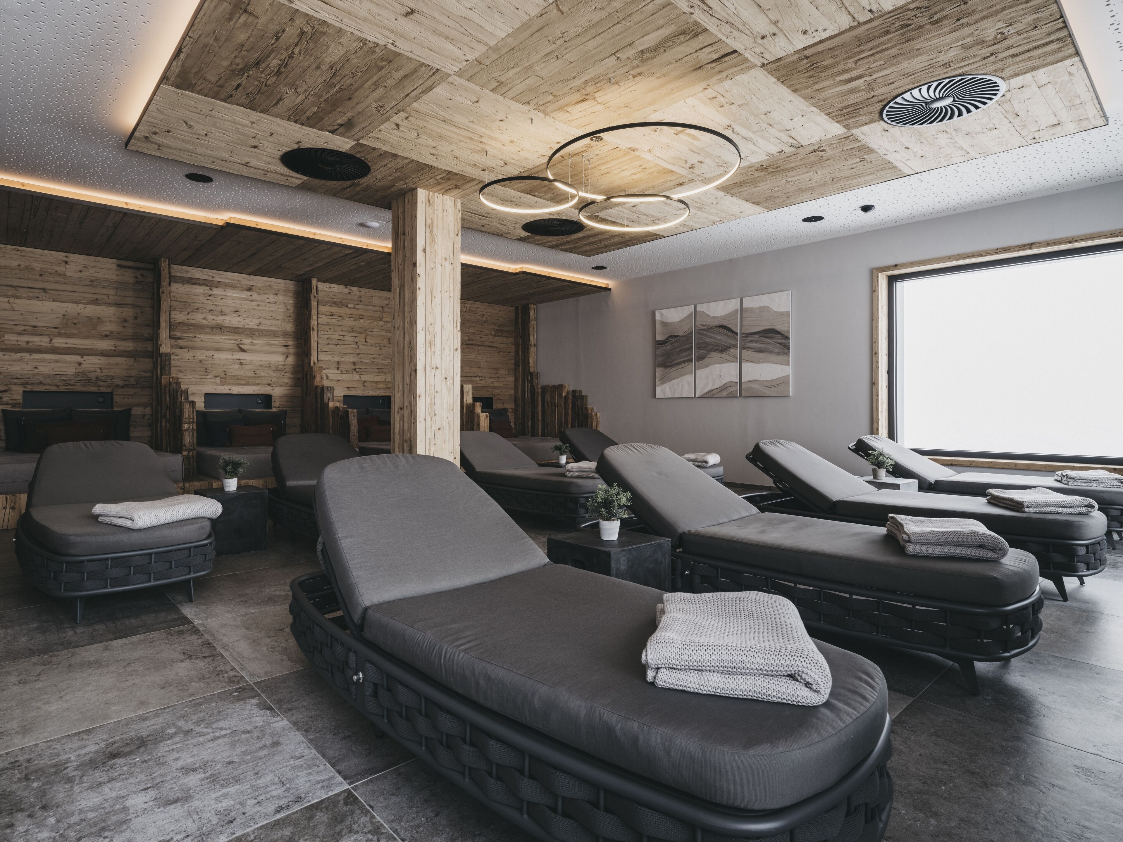Une salle de spa moderne avec des poutres en bois au plafond, des tables de massage et une grande fenêtre.