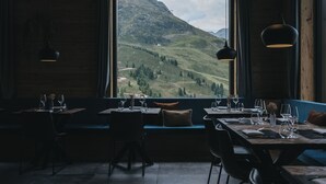 A restaurant with a large window offering a view of a mountainous landscape. Tables are set with wine glasses and plates. - VAYA Kühtai (Silz)