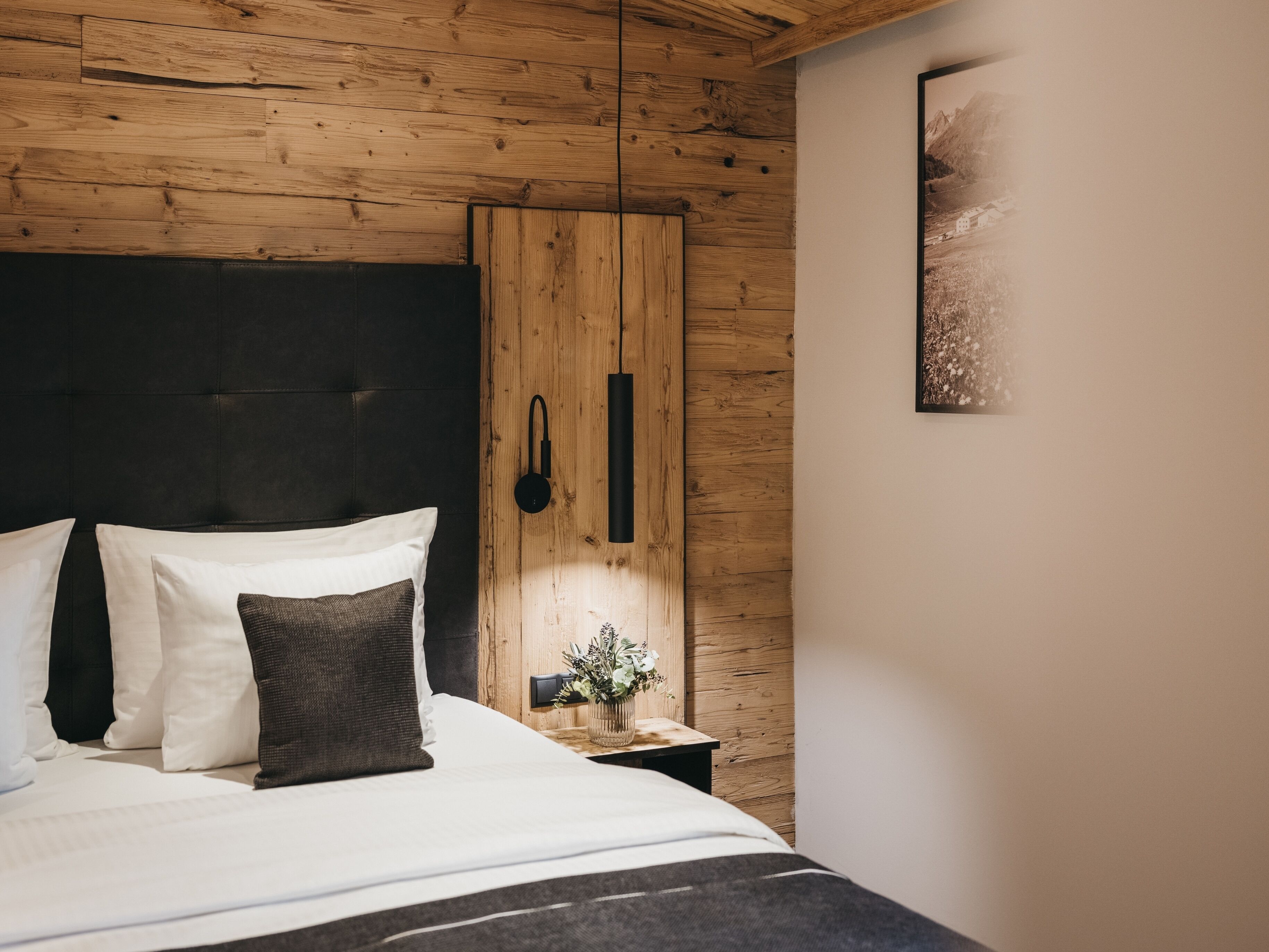 A bedroom with a wooden headboard, a bedside table with a plant, and a framed picture on the wall.