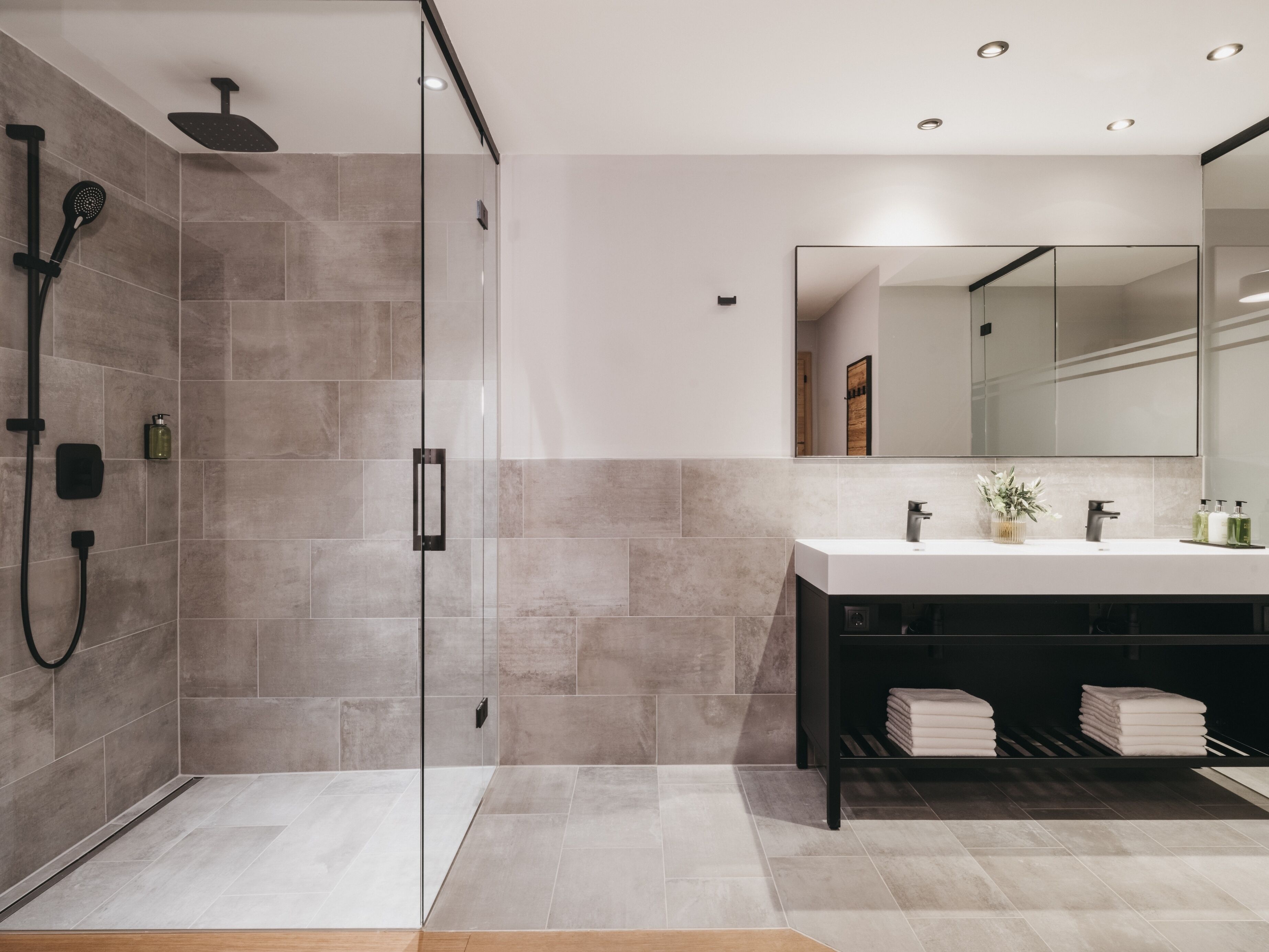 A modern bathroom with a glass shower enclosure, a large mirror, and a vanity with a sink and towel rack.
