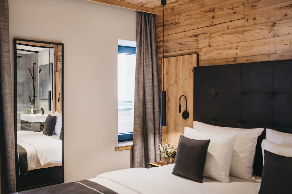 A modern bedroom with a large bed, a wooden ceiling, a mirror, and a window with curtains.