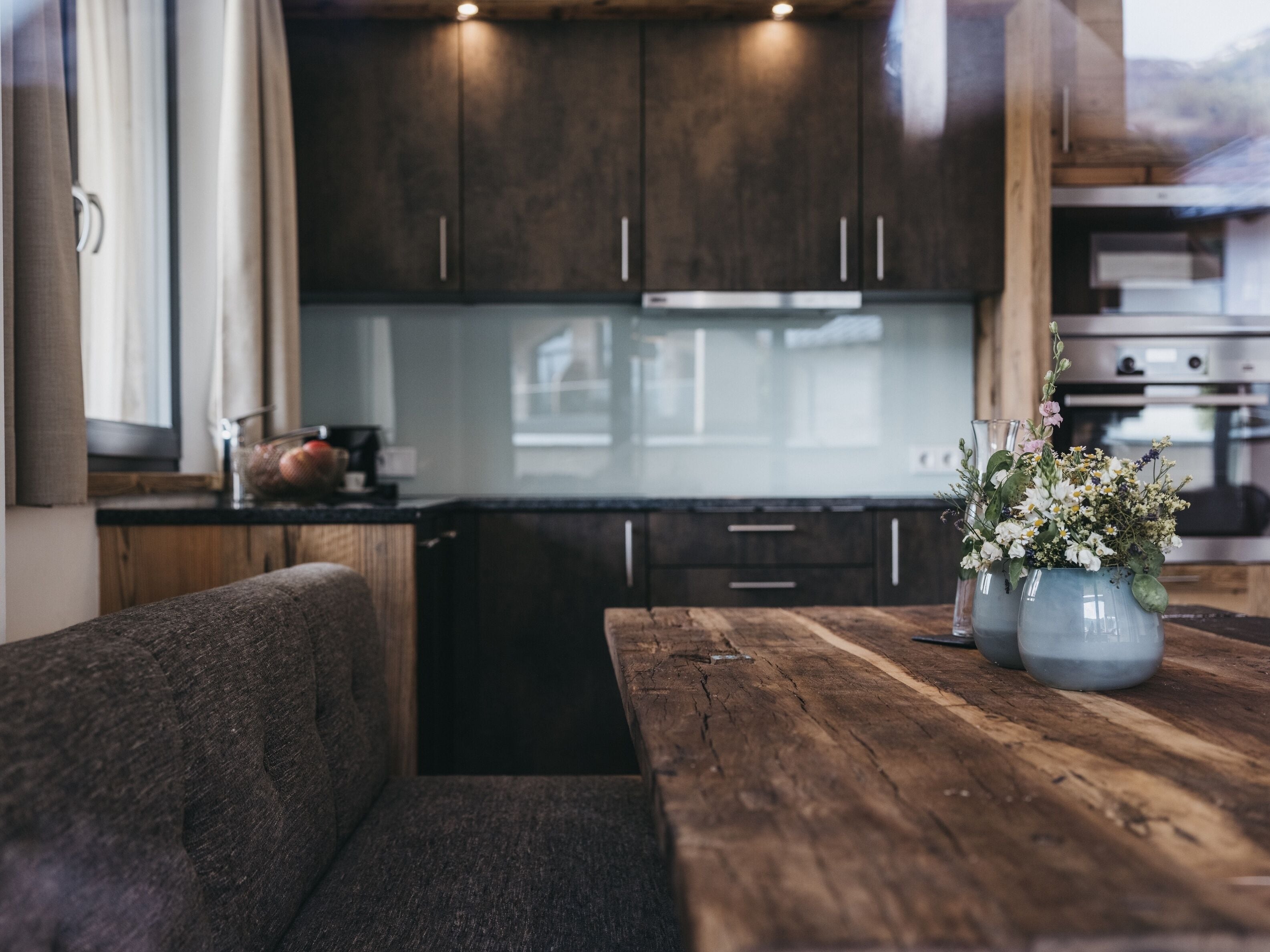 Una cocina moderna con armarios oscuros, una mesa de comedor de madera y un florero con flores.