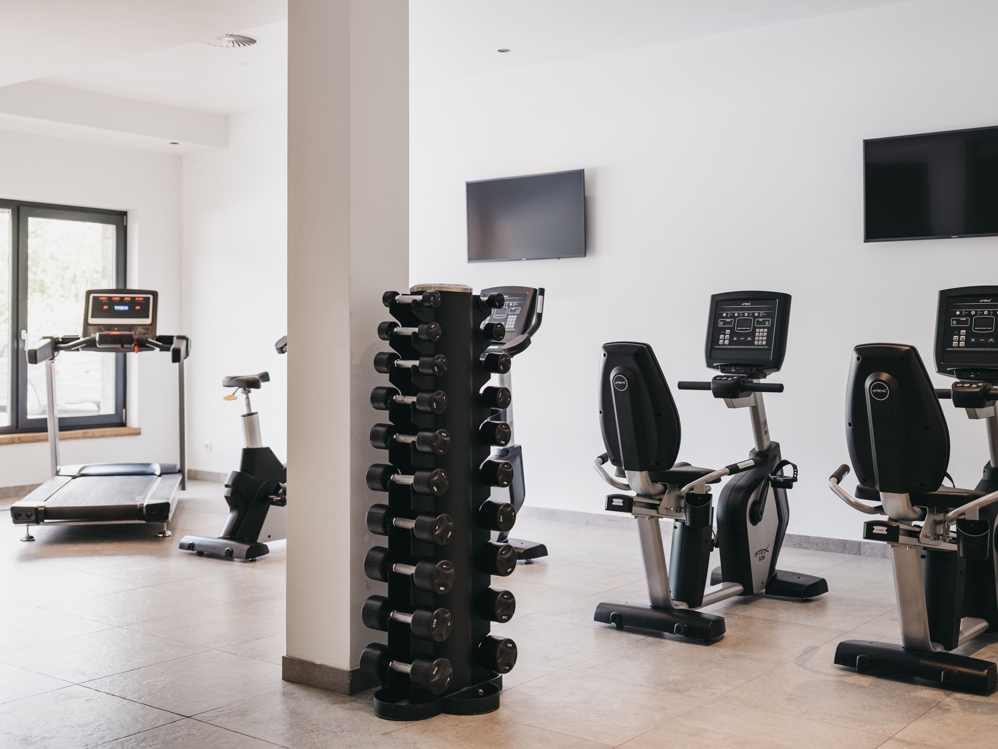 Ein Fitnessstudio mit Laufbändern, Crosstrainern und einer Hantelbank.