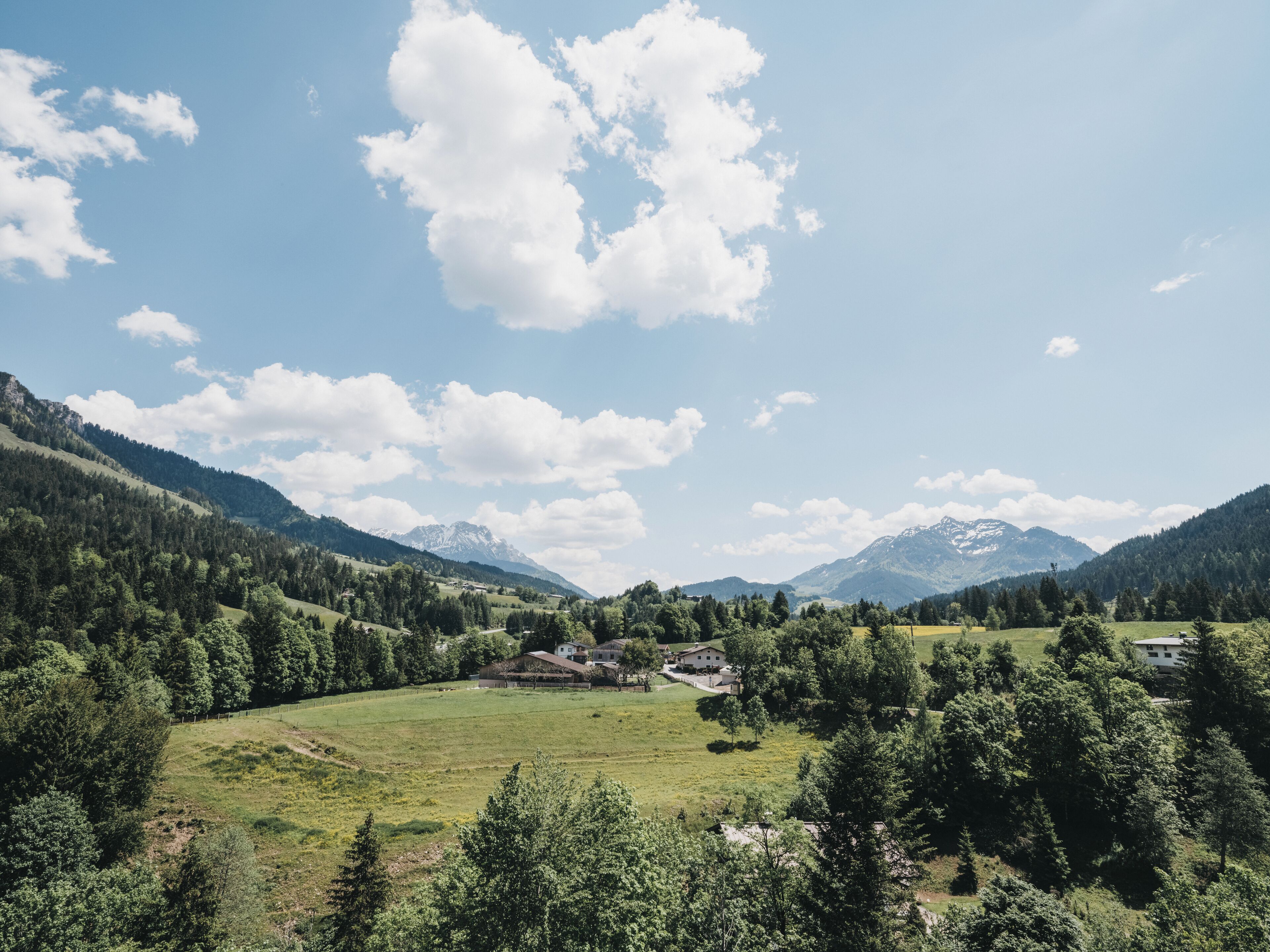 A rural landscape with a valley, mountains, and a few buildings.