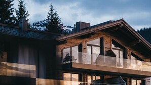 A modern multi-story building with large windows, wooden beams, and a balcony with outdoor seating.