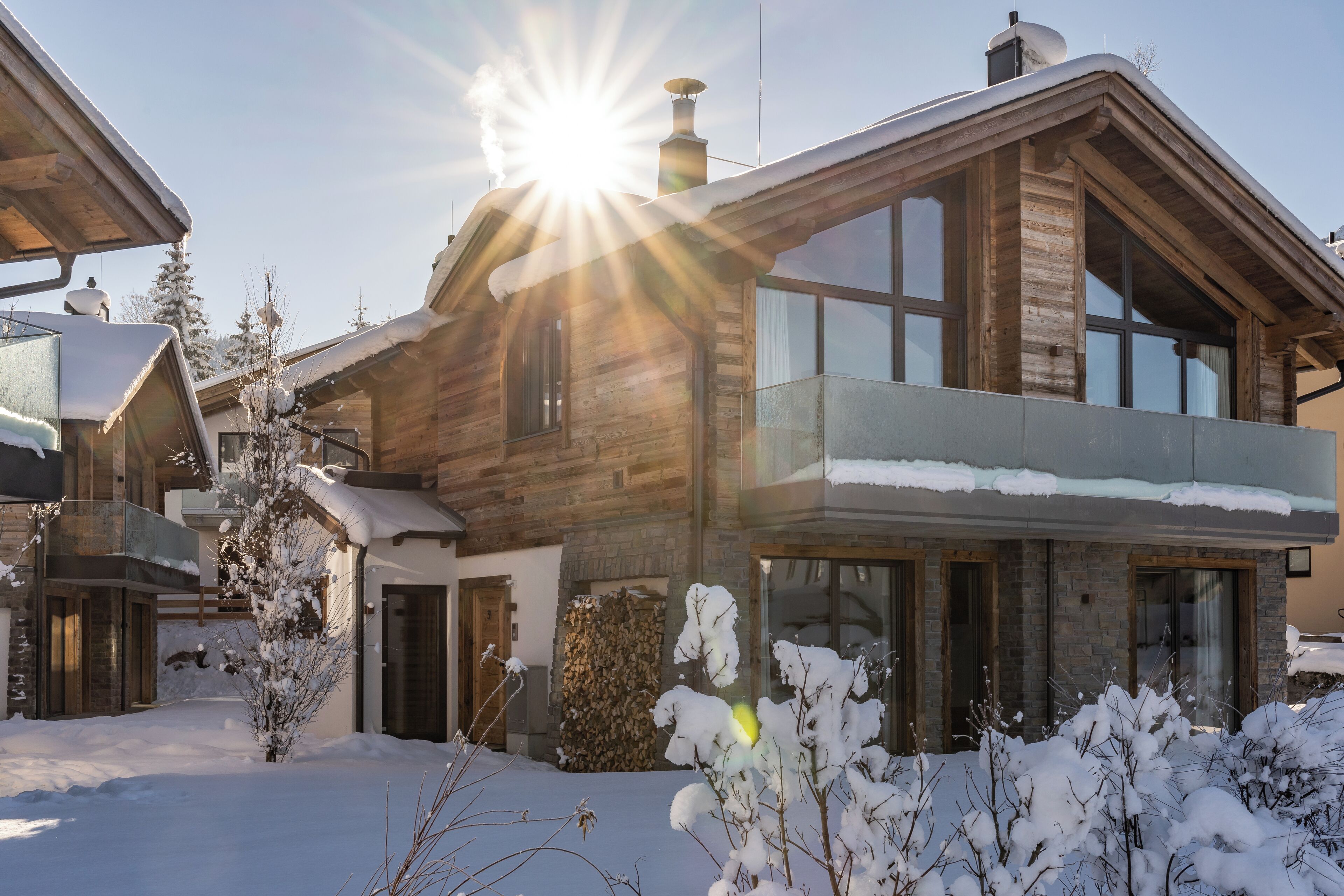 A wooden cabin with a balcony, a stone fireplace, and a snow-covered yard.