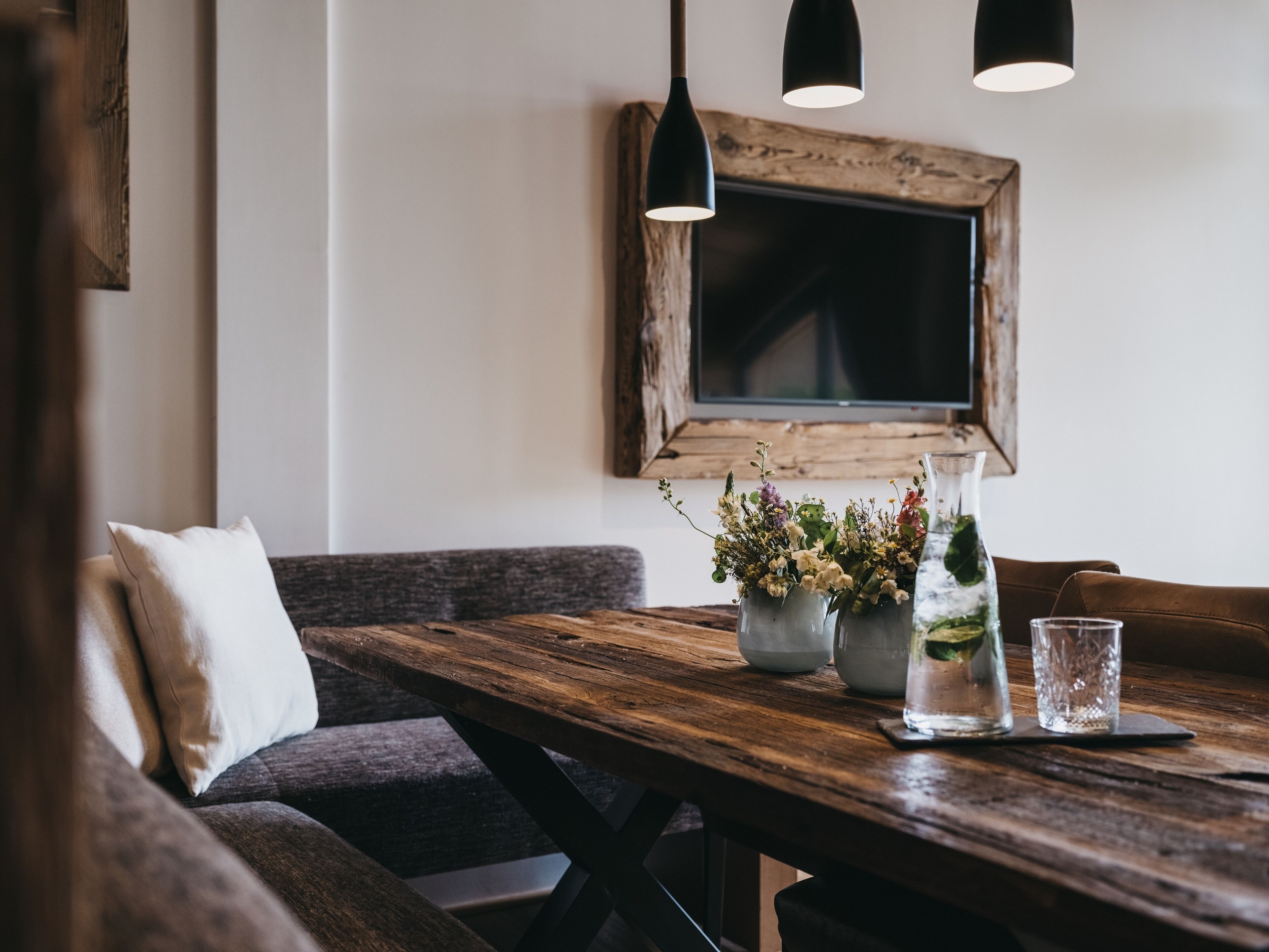 A rustic dining area with a wooden table, benches, and hanging pendant lights.