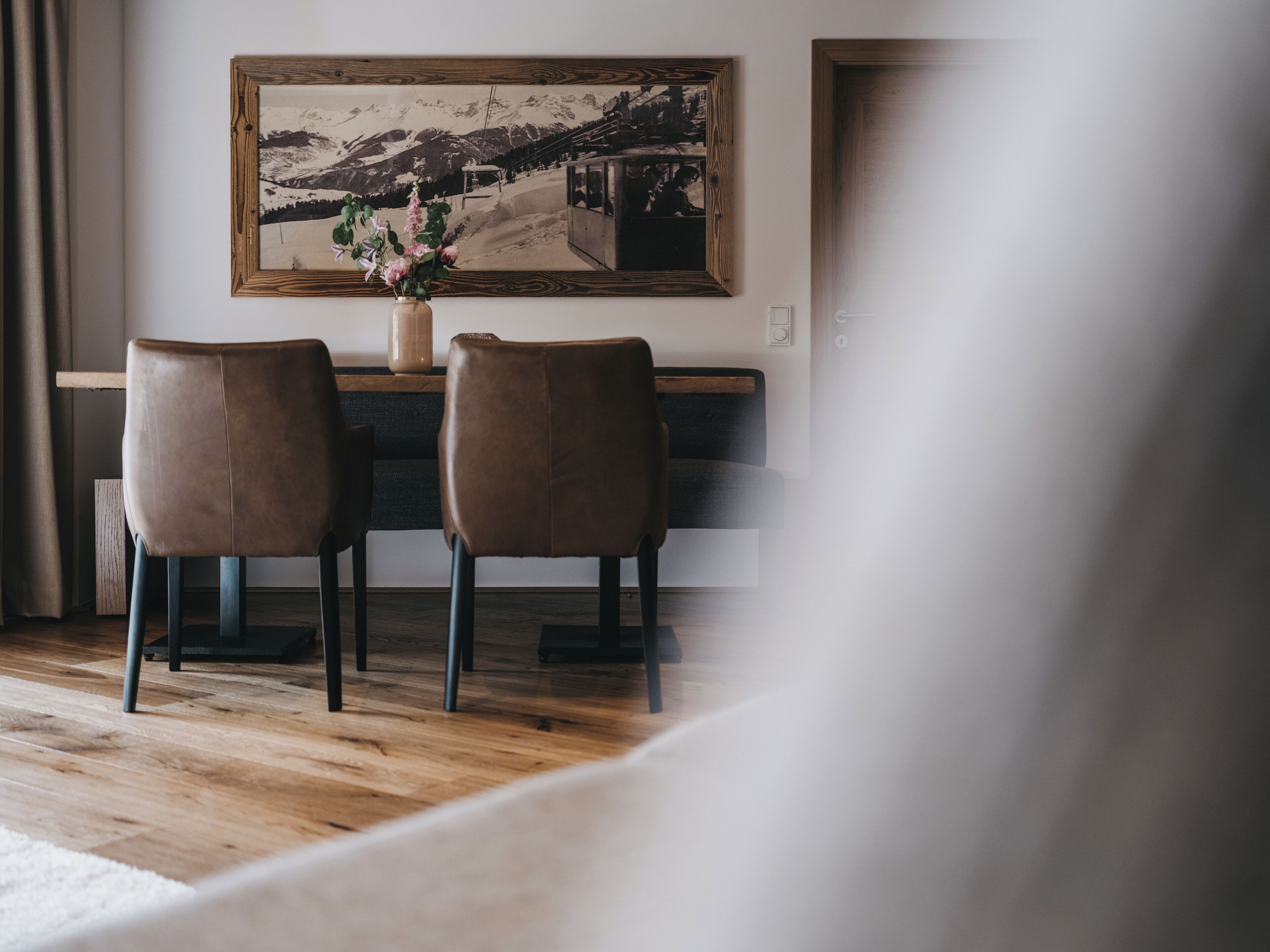 Un comedor con dos sillas y una mesa, un cuadro enmarcado en la pared, y suelo de madera.