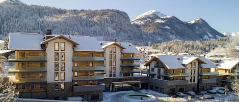 Ein mehrstöckiges Hotel mit einem Skigebiet im Hintergrund, ausgestattet mit einem Innenhof und einem Parkplatz.