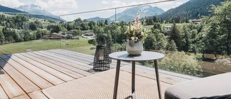 Una terraza de madera con una mesa redonda y una planta en maceta, con vistas a un paisaje montañoso.