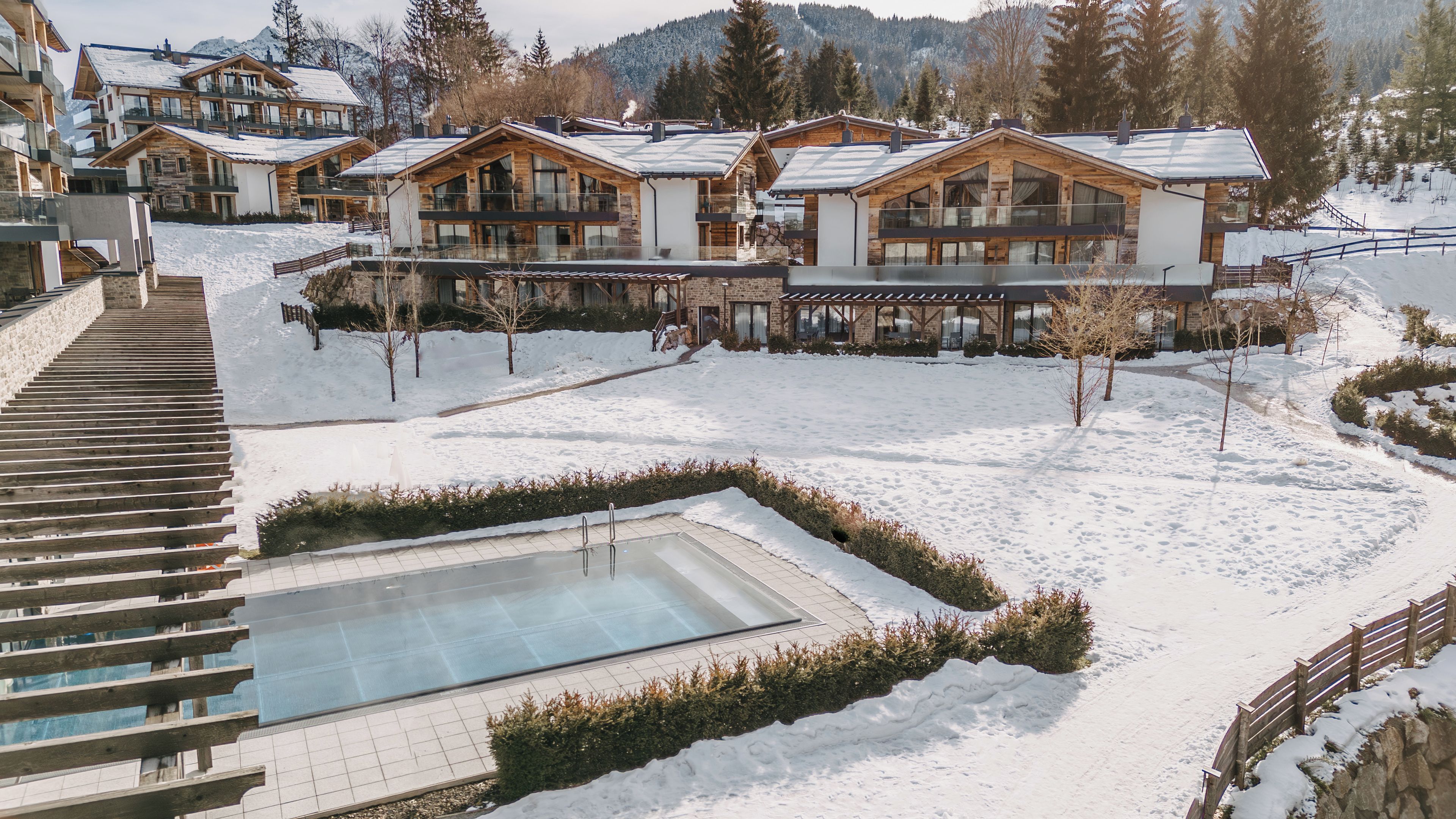 A snow-covered outdoor area with a pool, wooden buildings, and a staircase.