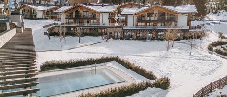 A snow-covered outdoor area with a pool, wooden buildings, and a staircase.
