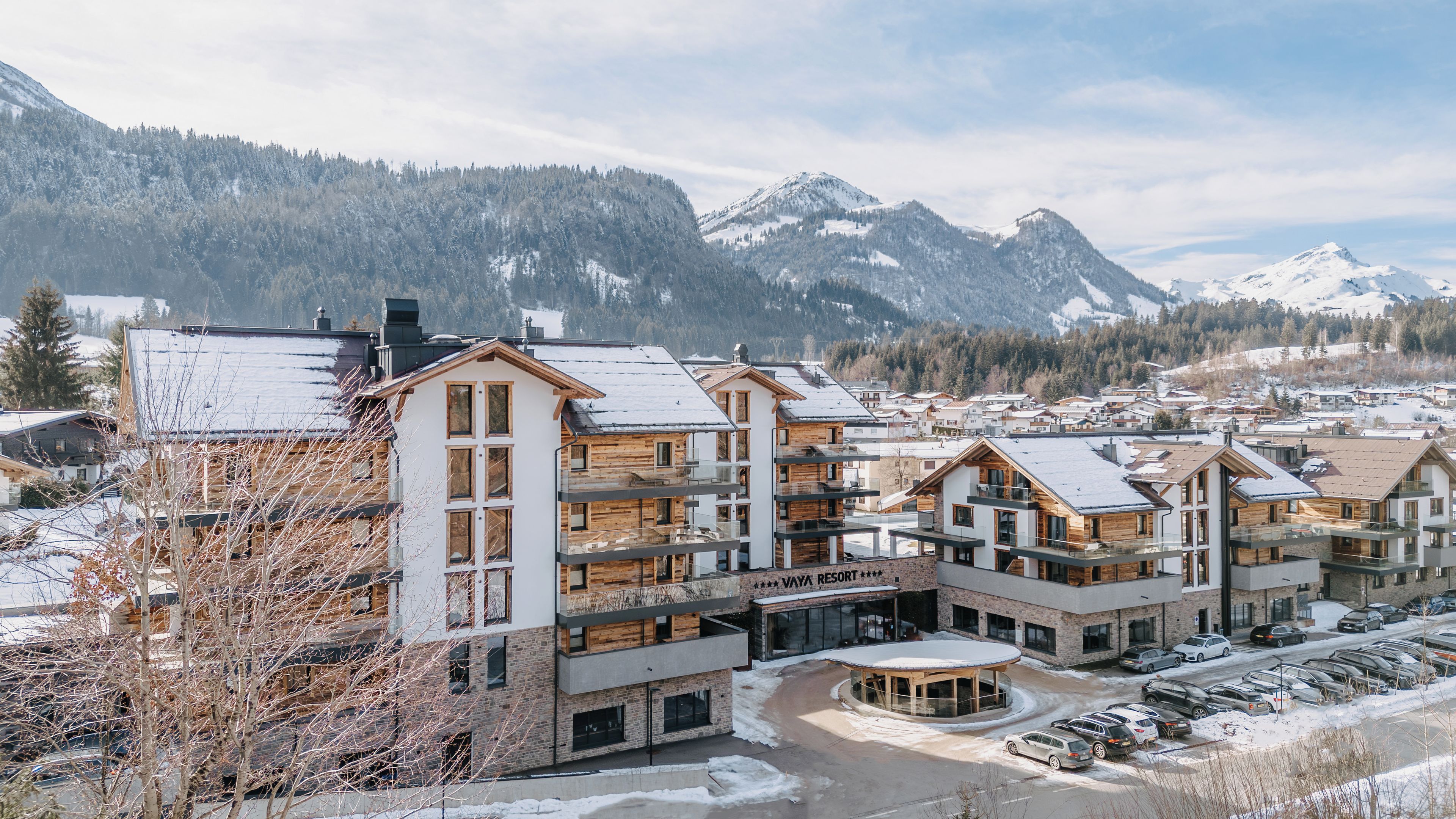 Une station de ski avec des bâtiments à plusieurs étages, un parking et, en arrière-plan, des montagnes enneigées.