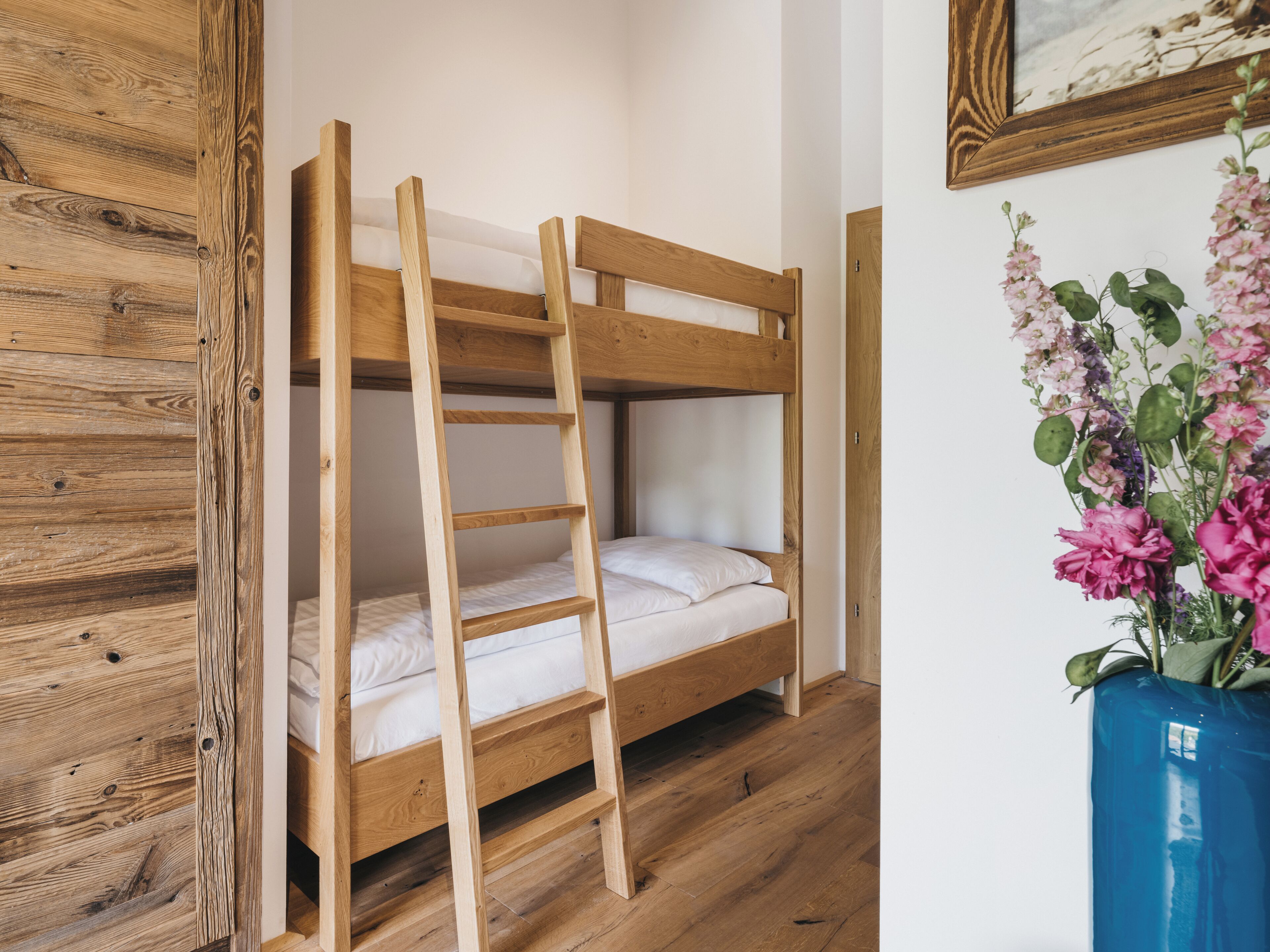 A bunk bed with a wooden ladder, white bedding, and a wooden wall.