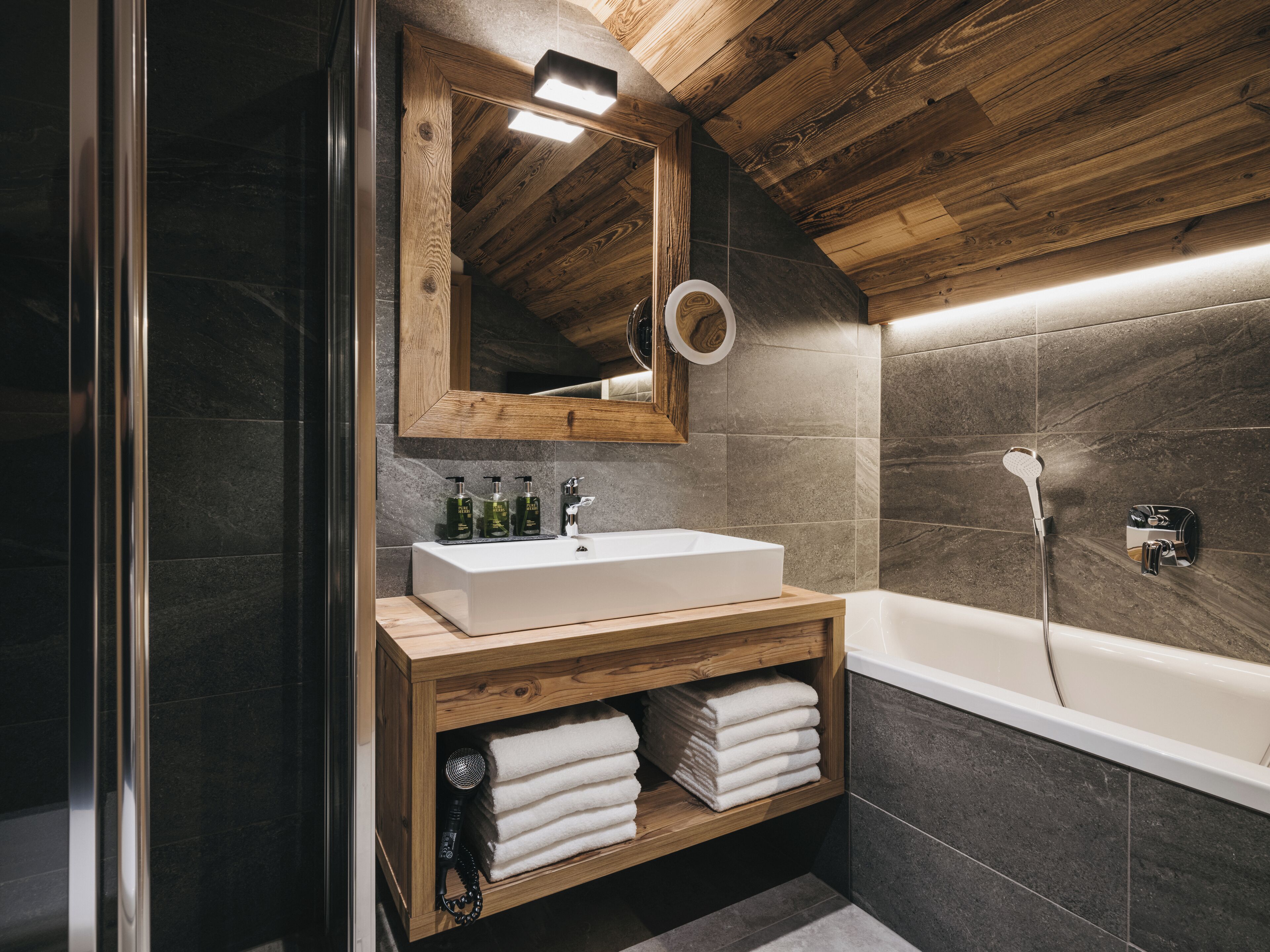 Un baño moderno con tocador de madera, un espejo grande y una bañera.