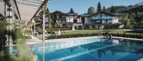 A modern hotel with a swimming pool, outdoor seating, and mountain views.