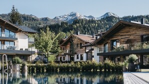 A modern resort with a pool reflecting the surrounding buildings and mountains.