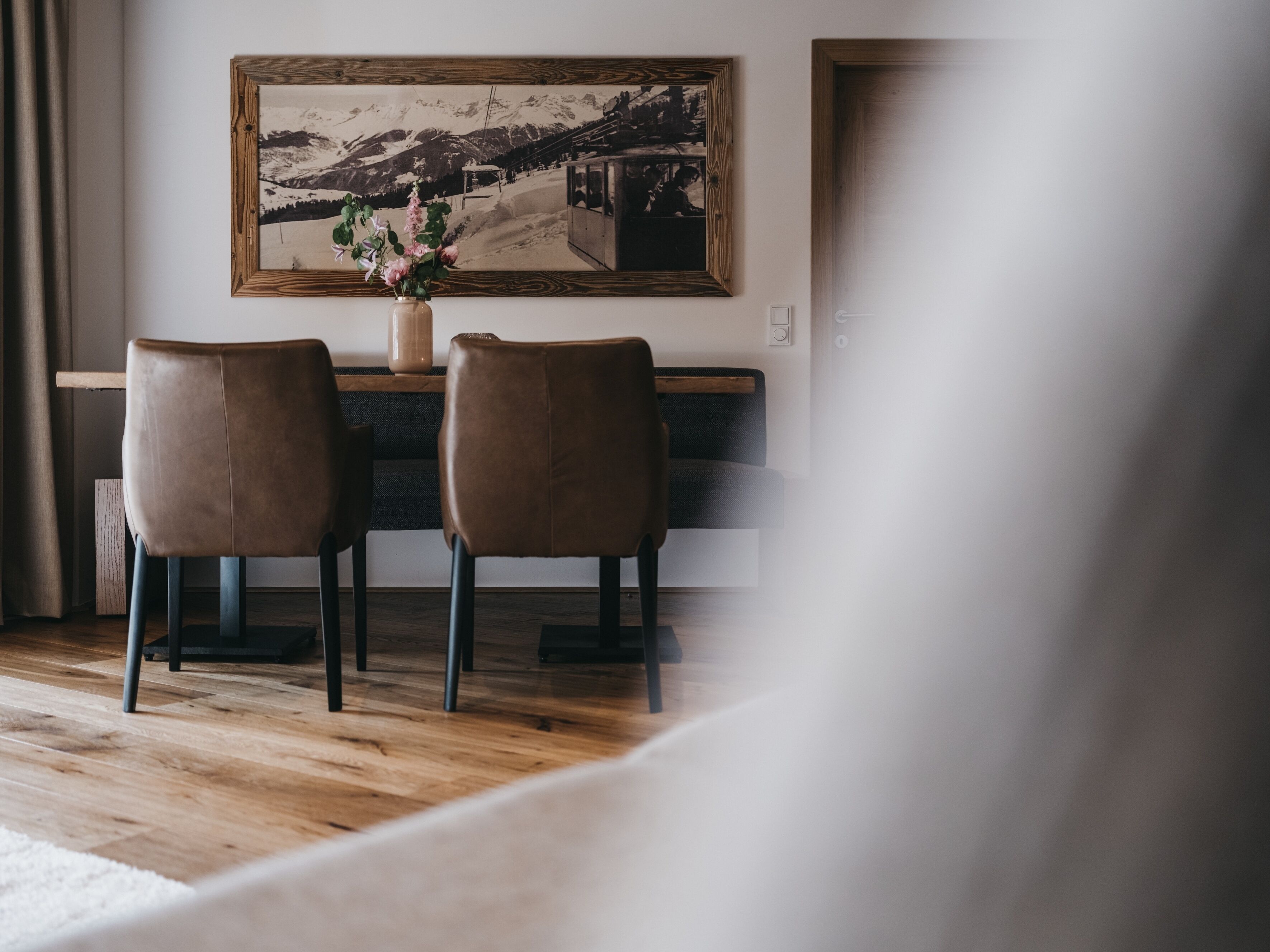 A dining area with two chairs, a table, and a painting on the wall.