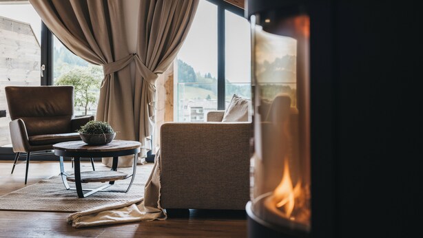 A cozy living room with a fireplace, a sofa, a chair, and a view of a cityscape through large windows.