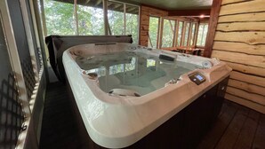 A hot tub in a wooden cabin with a view of trees through large windows. - NEW Games Added! Spacious Lodge, Theater Rm, NFL Sunday, 2 Pools, & FishingPond (Sevierville)