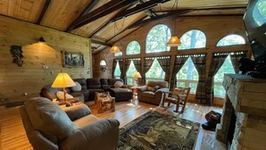 A cozy living room with a fireplace, wooden floors, and large windows. - NEW Games Added! Spacious Lodge, Theater Rm, NFL Sunday, 2 Pools, & FishingPond (Sevierville)