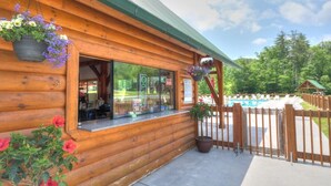 A wooden cabin with a glass door, a small outdoor seating area, and a view of a pool. - NEW Games Added! Spacious Lodge, Theater Rm, NFL Sunday, 2 Pools, & FishingPond (Sevierville)