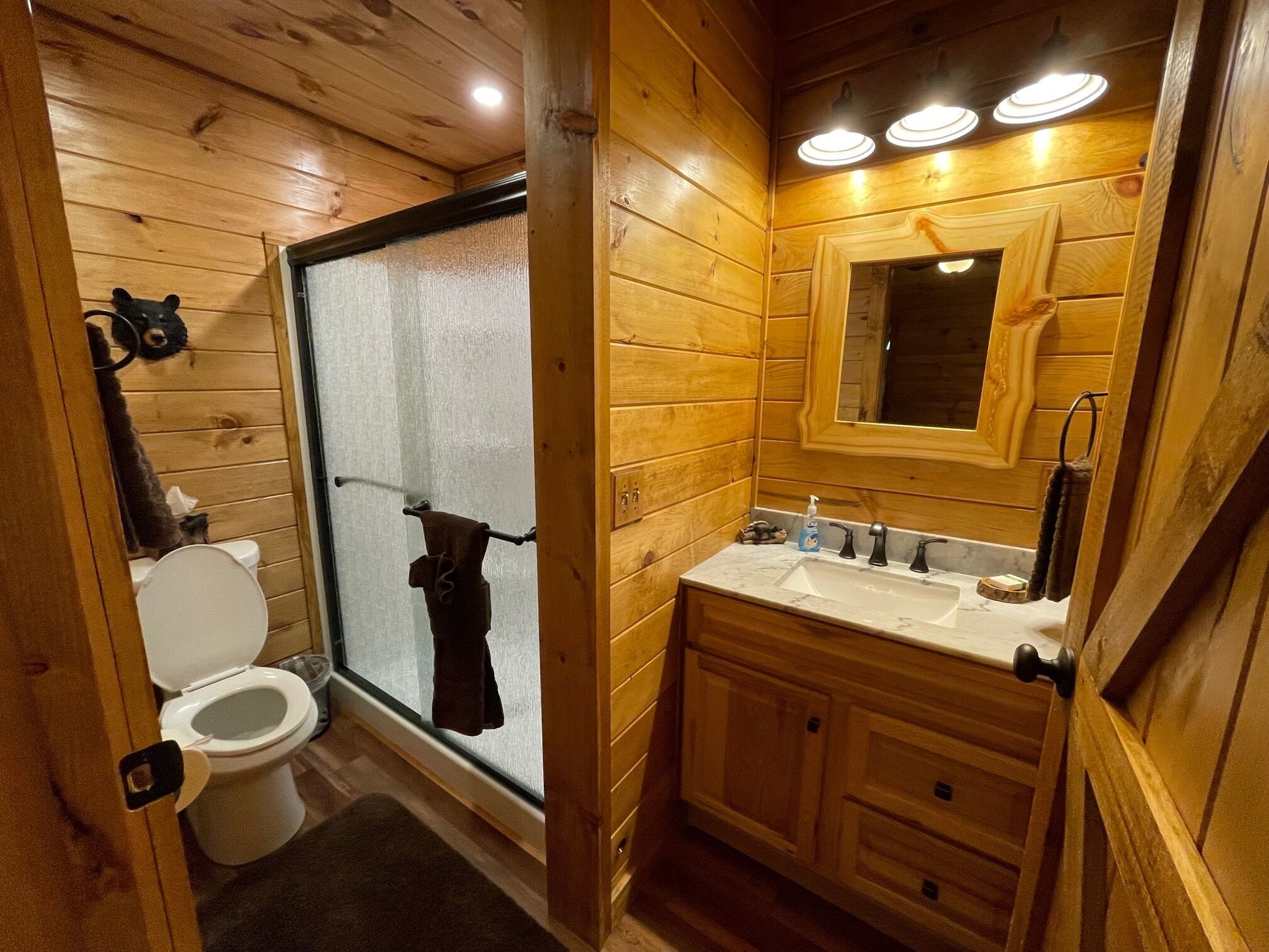 Baño de cabaña de madera con inodoro, ducha, lavabo y espejo.