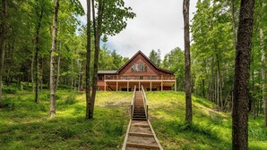 Une cabane en bois dotée d’une terrasse centrale et d’un escalier menant à l’entrée, le tout entouré d’une forêt.