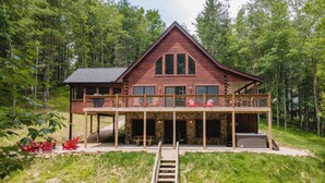 Une cabane en rondins à deux étages, dotée d’un balcon, d’un espace salon extérieur et d’un escalier menant à l’entrée.