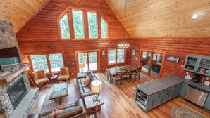Un intérieur spacieux de chalet en bois, comprenant un salon, un coin repas, une cuisine et une cheminée en pierre.