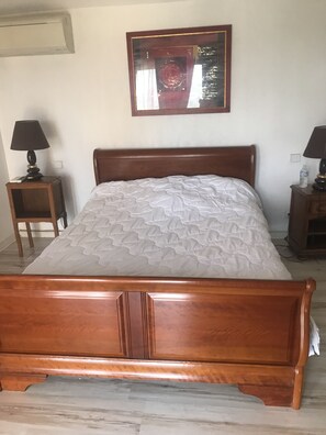 Una cama de madera con colcha blanca, dos mesitas de noche con lámparas y una obra de arte enmarcada en la pared.