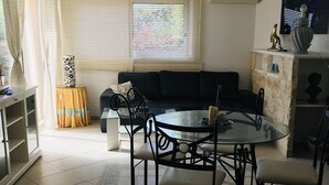 En matplats med ett glasbord och stolar, en soffa, ett skåp och ett fönster med persienner.