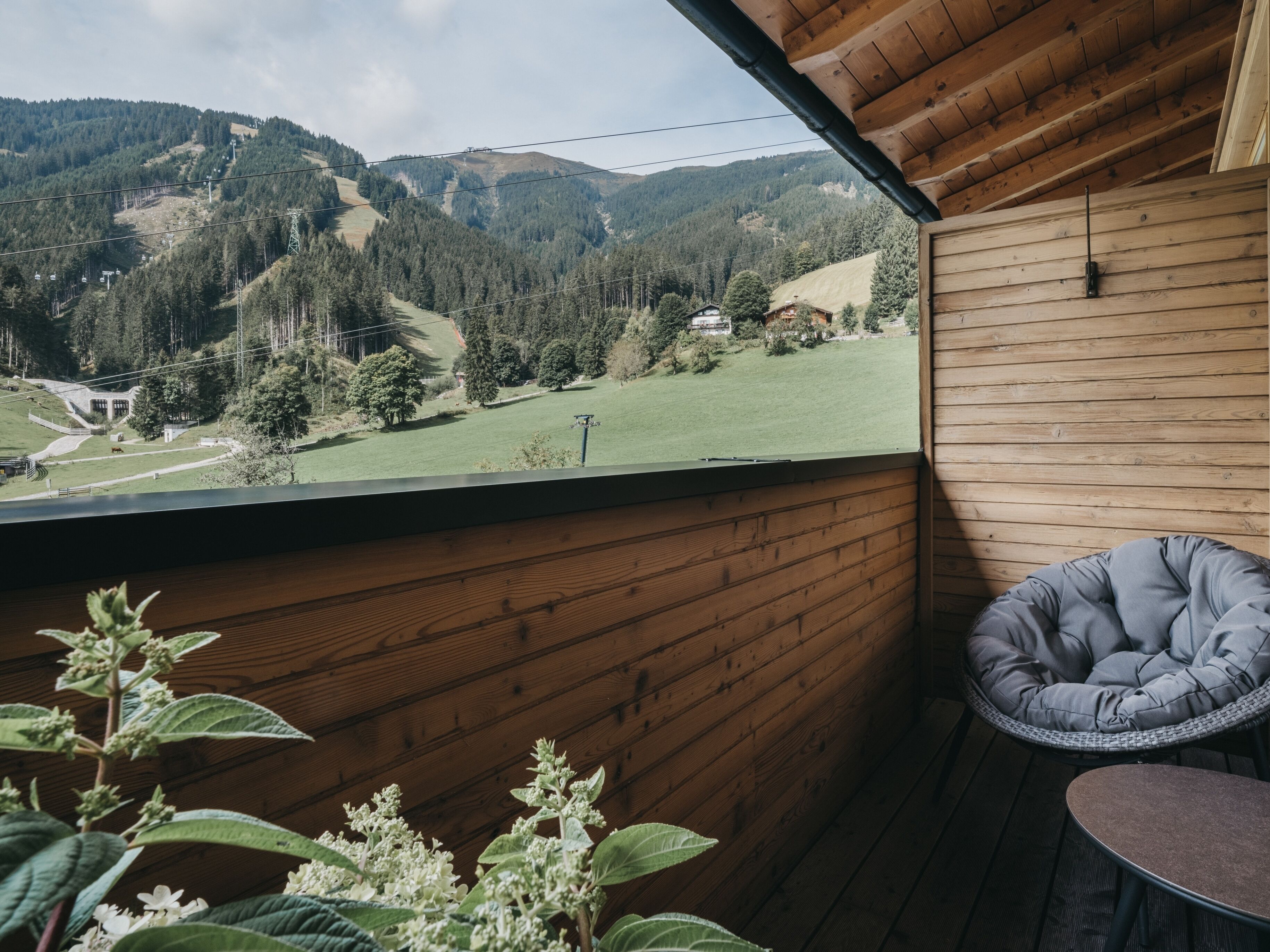 A wooden balcony with a view of a green valley and mountains.
