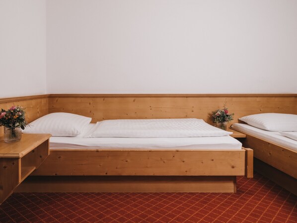 Una cama de madera con ropa de cama blanca en una habitación con suelo rojo estampado.