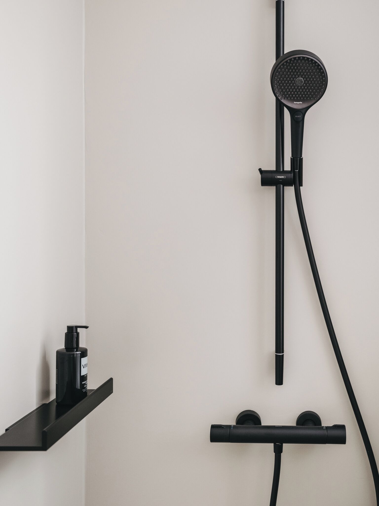 Een moderne badkamer met een zwarte douchekop, een handdouche en een zeepdispenser op een zwarte plank.