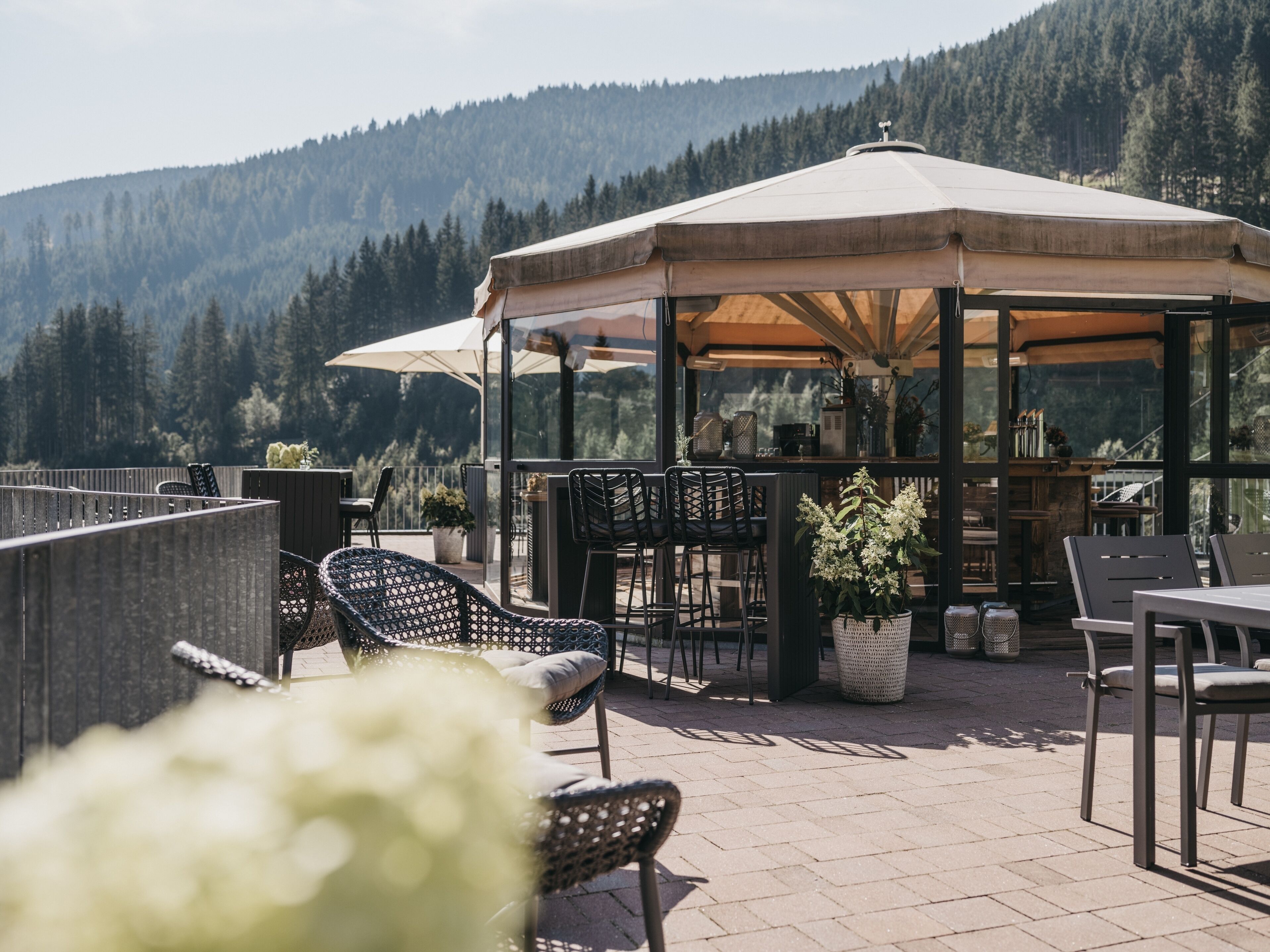 An outdoor patio with chairs and tables, a covered seating area, and a view of a forested mountain.