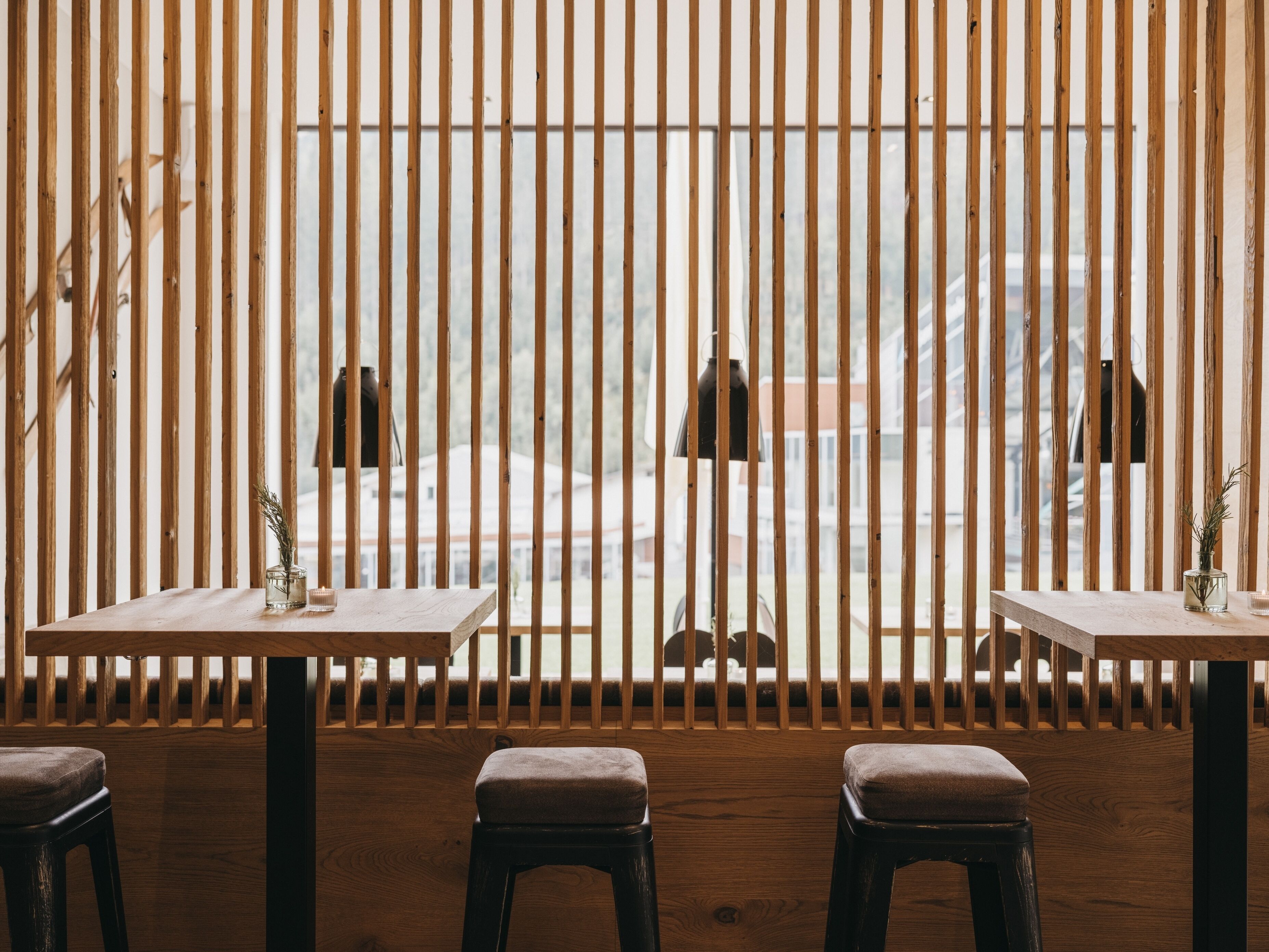 A restaurant with wooden slats, two tables with candles, and a view of a building through the slats.