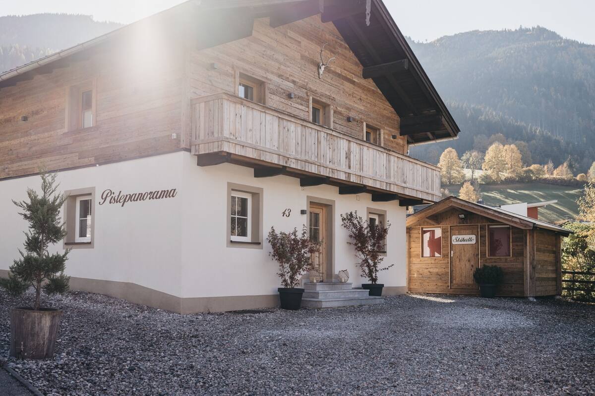 A traditional wooden chalet with a balcony, labeled "Pistepanorama," set against a mountainous backdrop.