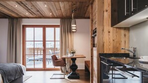 A modern hotel room with a wooden ceiling, a dining area with a table and chairs, and a kitchen with a countertop and sink. - VAYA Kaprun (Kaprun)