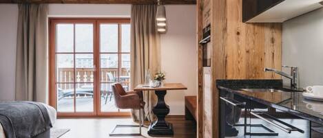 Habitación de hotel moderna con techo de madera, zona de comedor con mesa y sillas, y cocina con encimera y fregadero.